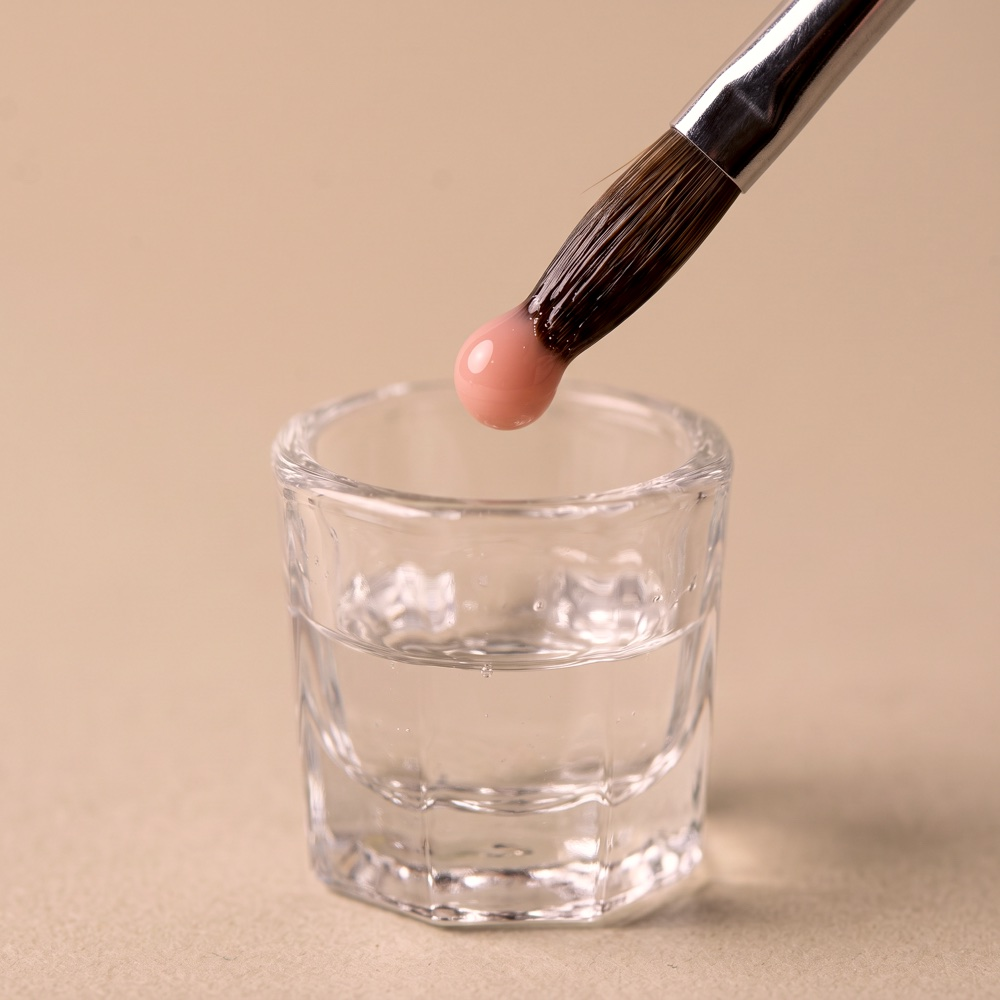 An acrylic brush holding a bead of product over a dish of monomer