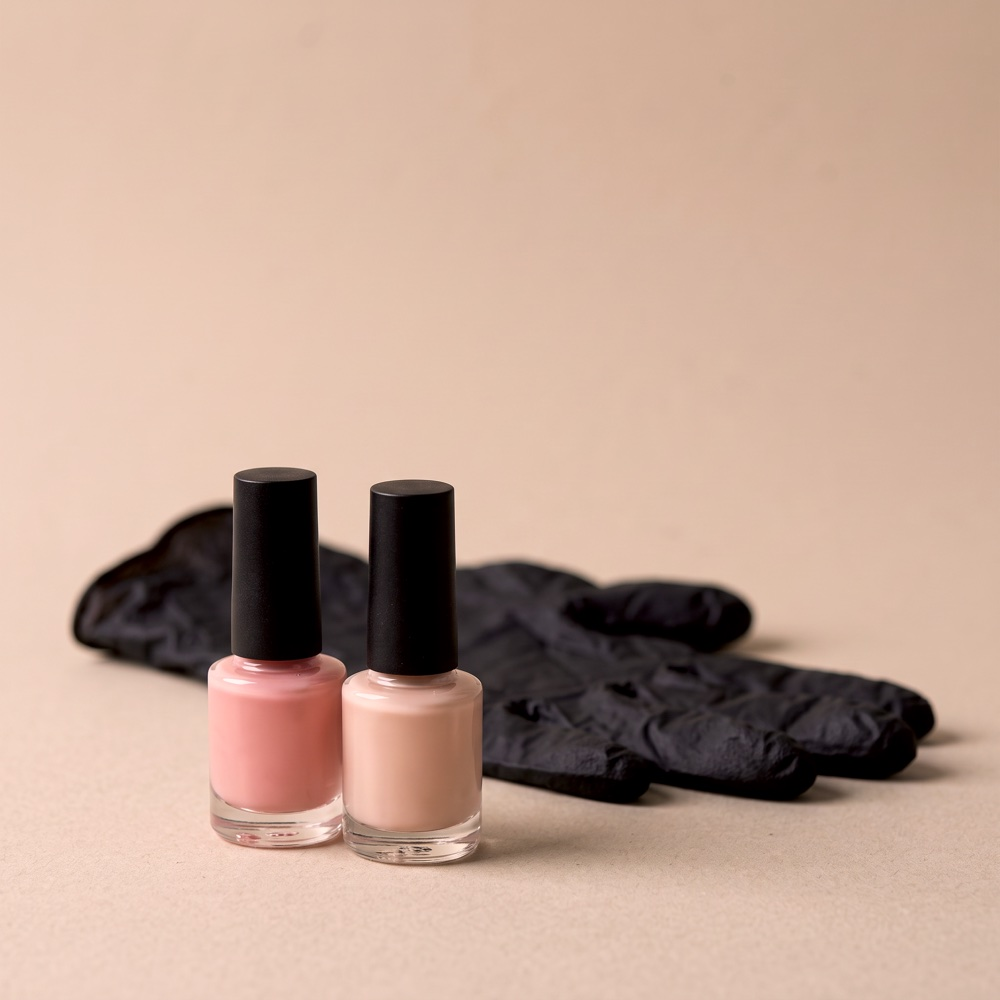 Two bottles of gel polish, pink and nude, in front of a black glove